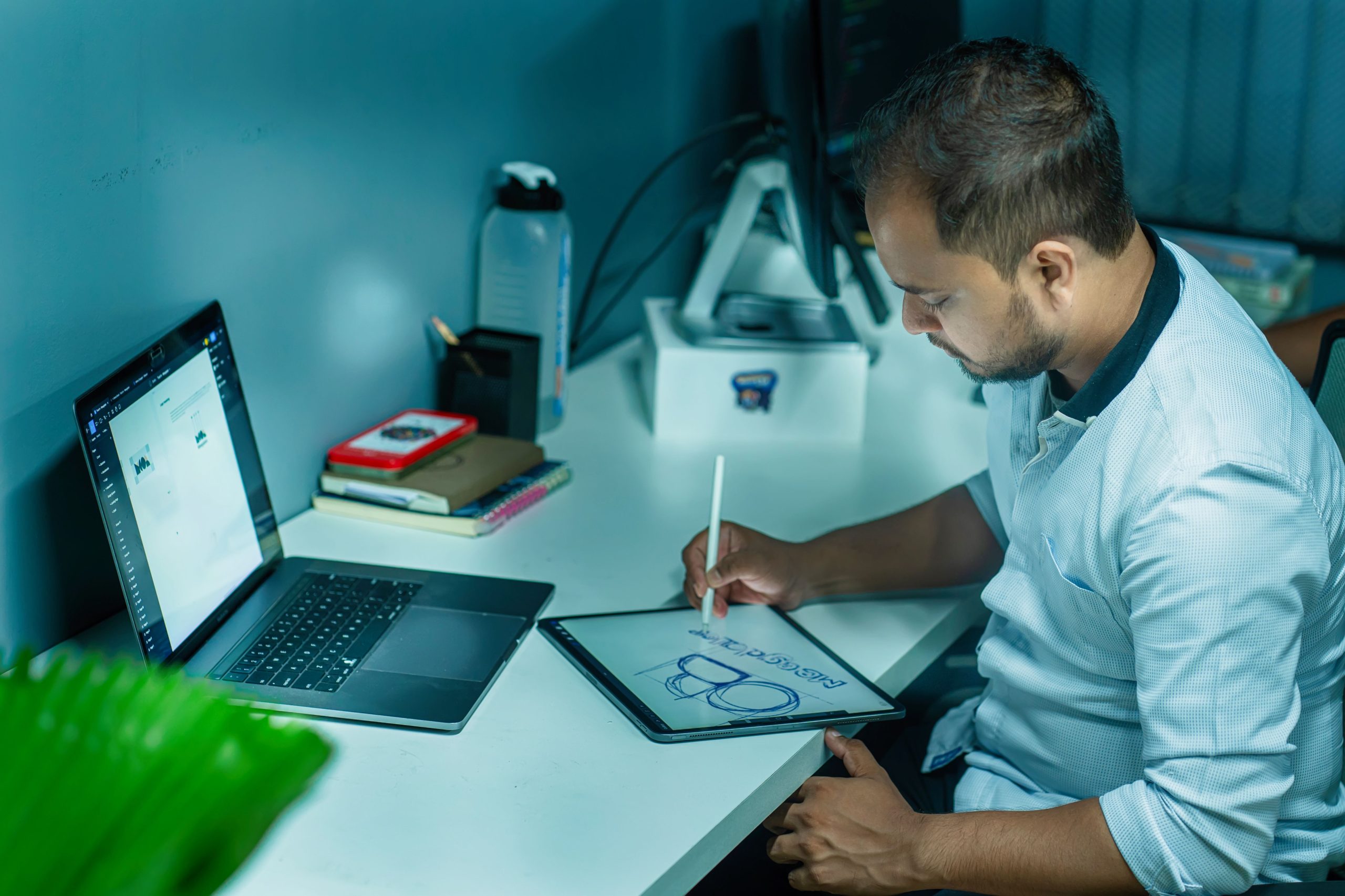 A focused man uses a tablet to design while working at his desk in a modern office setting.